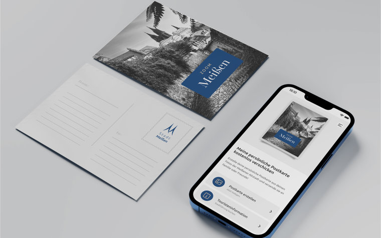 Postkarte mit Motiv aus der PWA ZOOMMEIßEN neben Smartphone