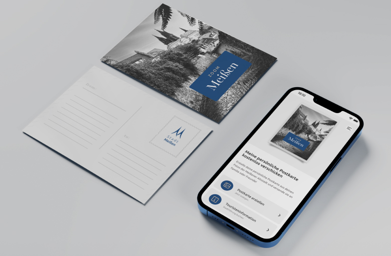 Postkarte mit Motiv aus der PWA ZOOMMEIßEN neben Smartphone